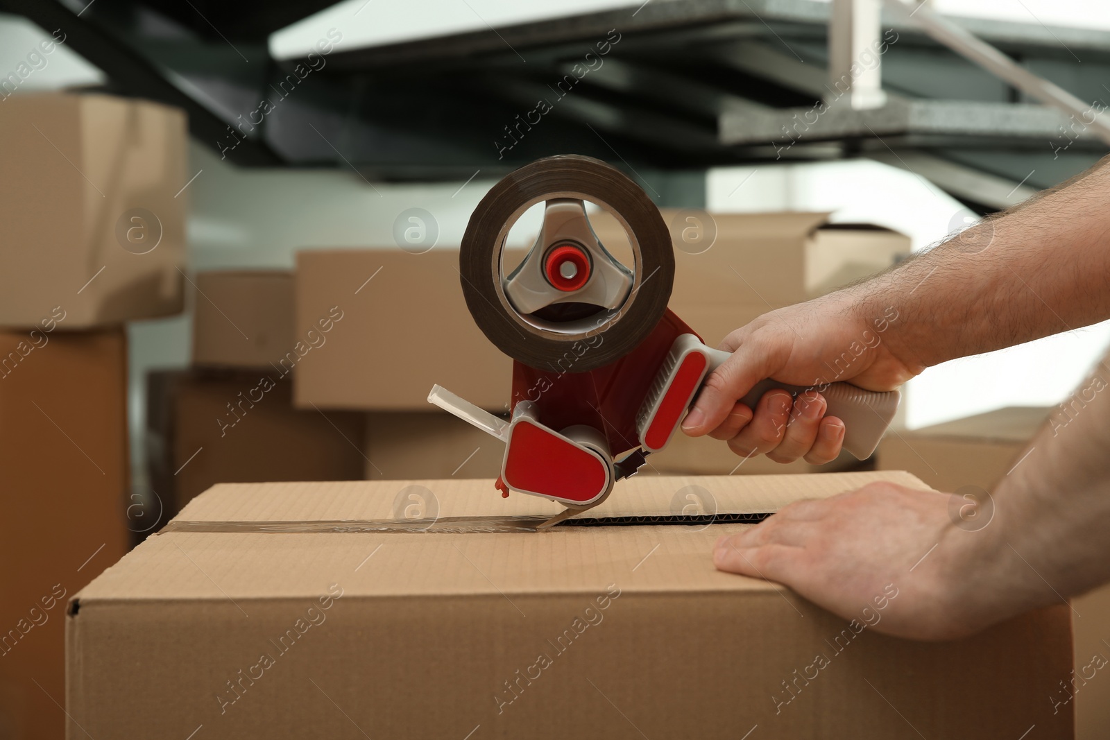 Photo of Worker taping cardboard box indoors, closeup view