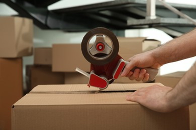 Worker taping cardboard box indoors, closeup view