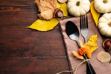 Seasonal table setting, space for text. Cutlery with pumpkins and autumn leaves on wooden background, flat lay