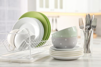 Photo of Many different clean dishware, cups and cutlery on white marble table in kitchen
