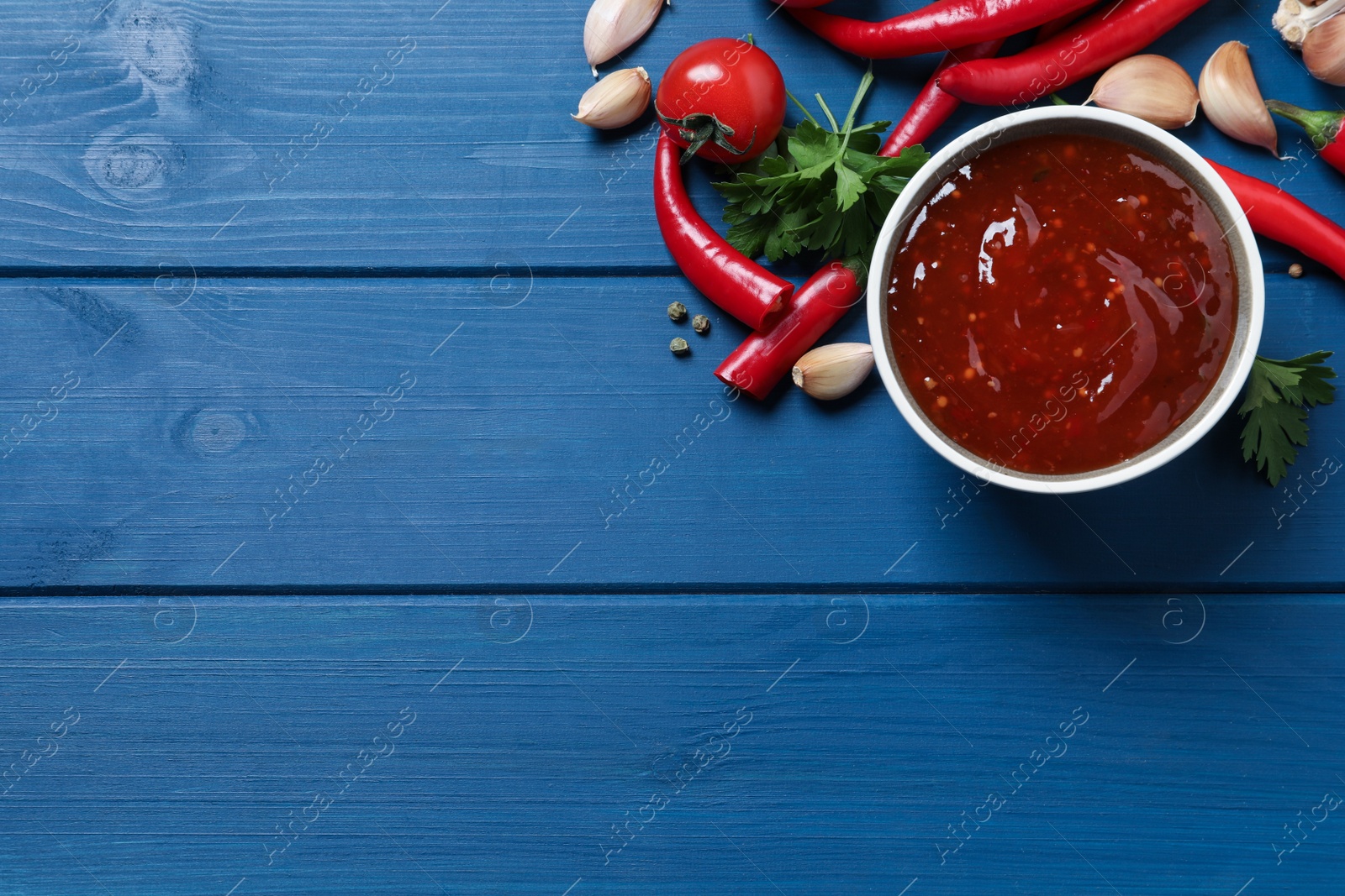 Photo of Spicy chili sauce and ingredients on blue wooden table, flat lay. Space for text