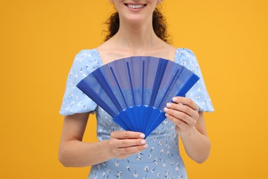 Woman holding hand fan on orange background, closeup