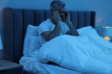 Mature man suffering from headache in bed at night