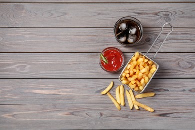 Photo of Tasty French fries, soda and ketchup on grey wooden table, flat lay. Space for text
