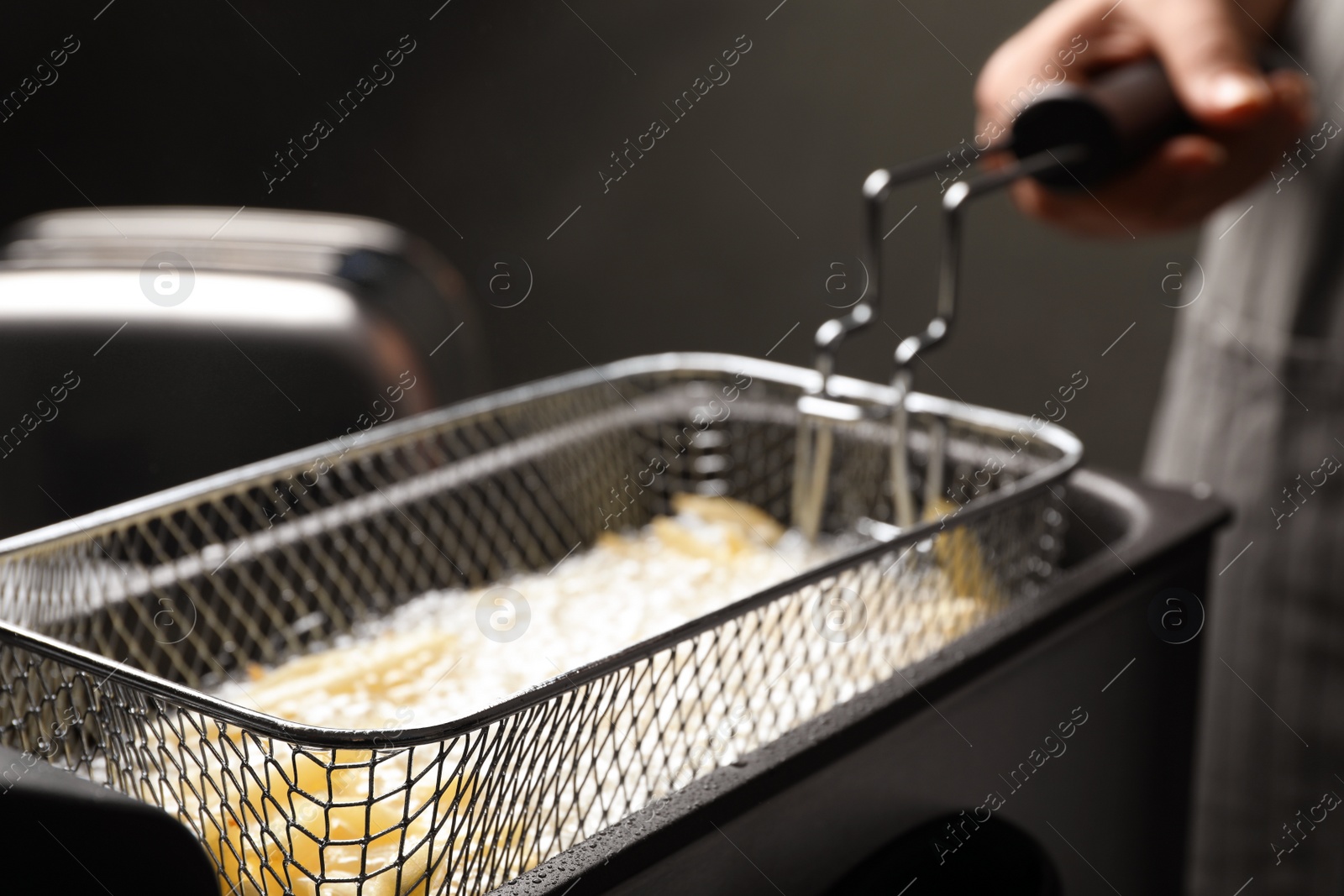 Photo of Chef cooking delicious french fries in hot oil, closeup