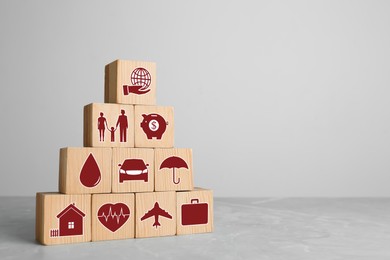 Wooden cubes with different icons on light grey table, space for text. Insurance concept