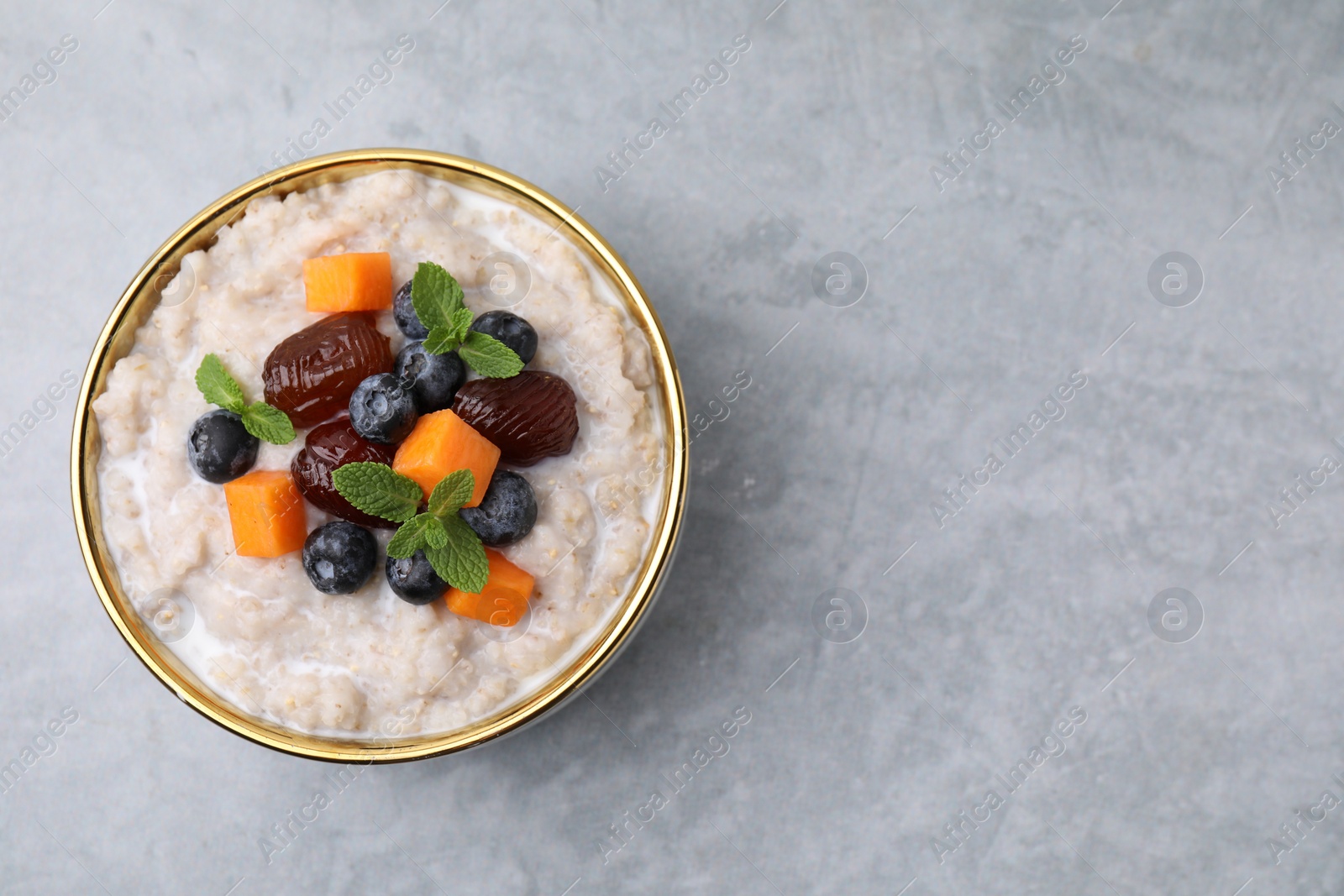 Photo of Delicious barley porridge with blueberries, pumpkin, dates and mint in bowl on grey table, top view. Space for text