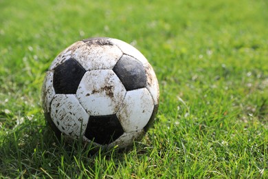 Dirty soccer ball on green grass outdoors, space for text