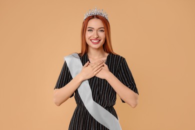 Photo of Beautiful young woman with tiara and ribbon in dress on beige background. Beauty contest