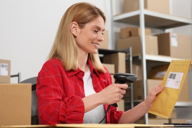 Photo of Seller with scanner reading parcel barcode at table in office. Online store