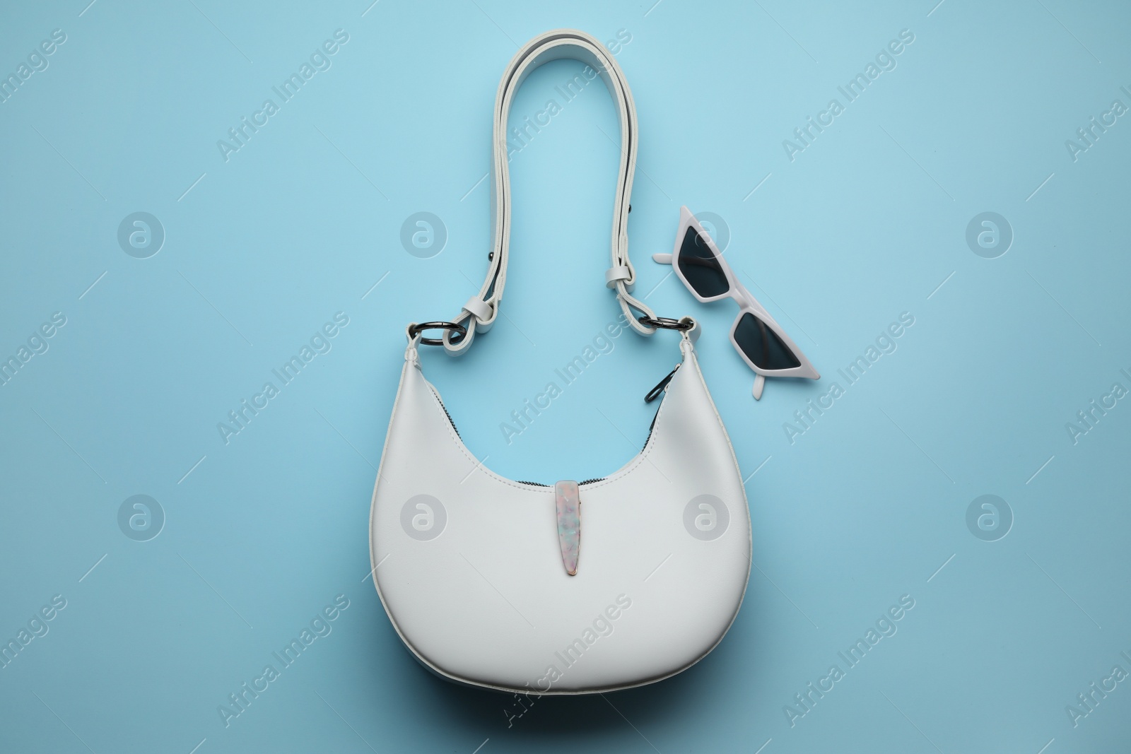 Photo of Stylish woman's bag and sunglasses on light blue background, flat lay