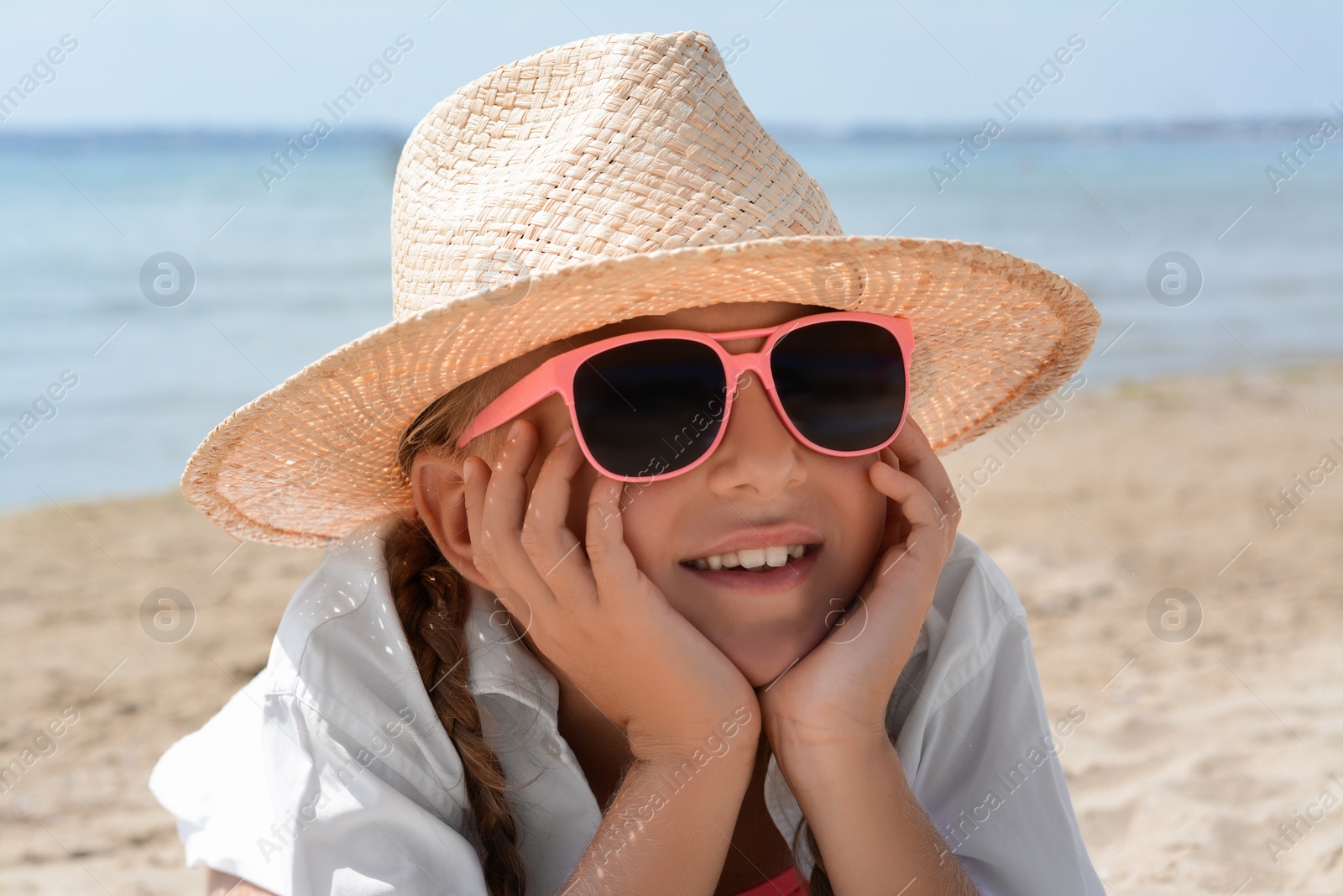 Photo of Little girl wearing sunglasses and hat at beach on sunny day