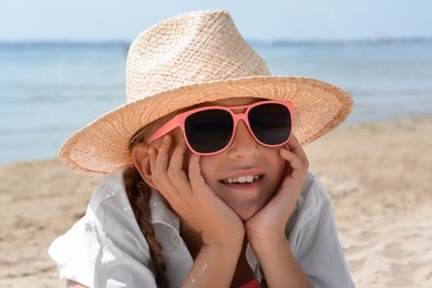 Little girl wearing sunglasses and hat at beach on sunny day