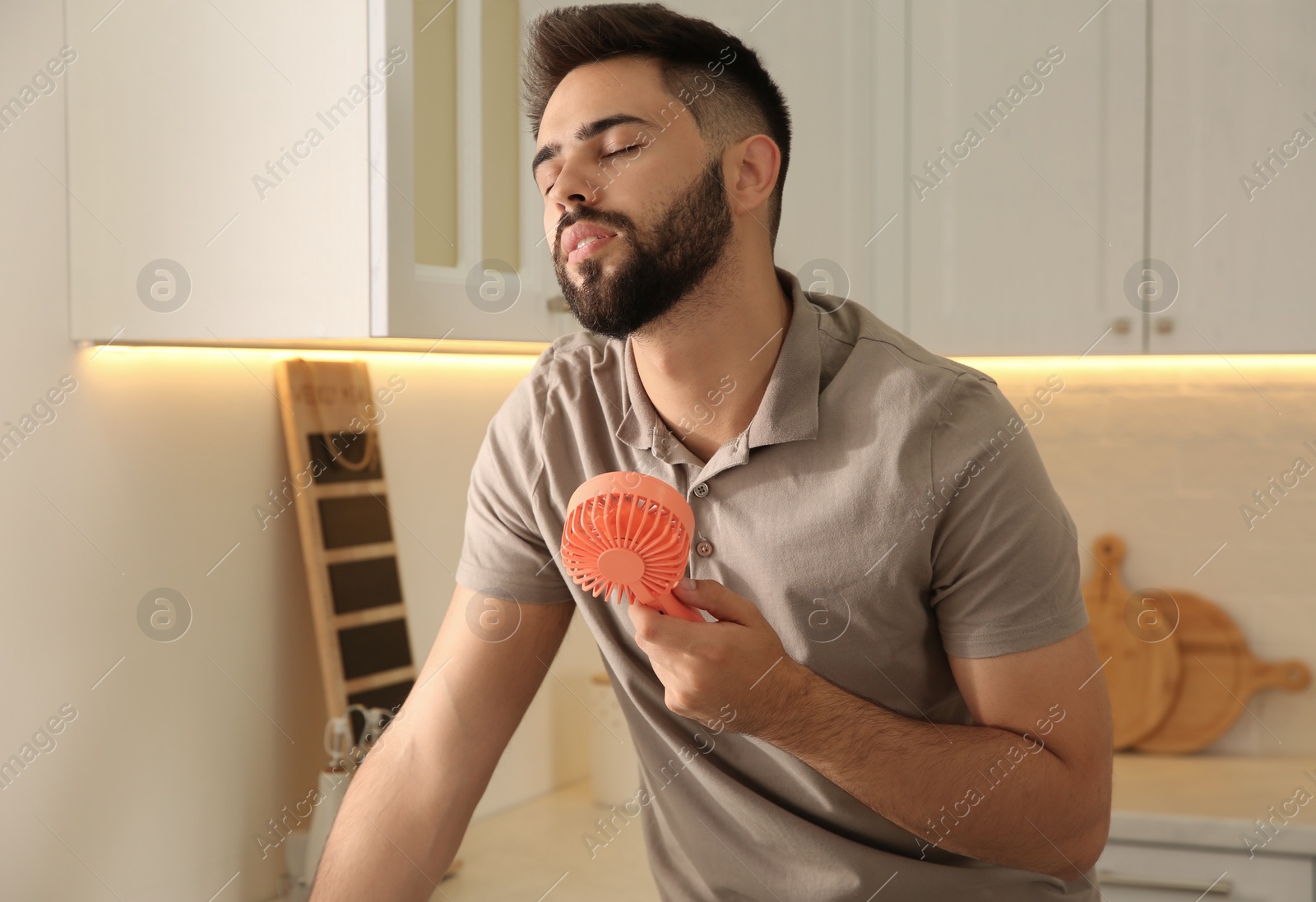 Photo of Man enjoying air flow from portable fan at home. Summer heat