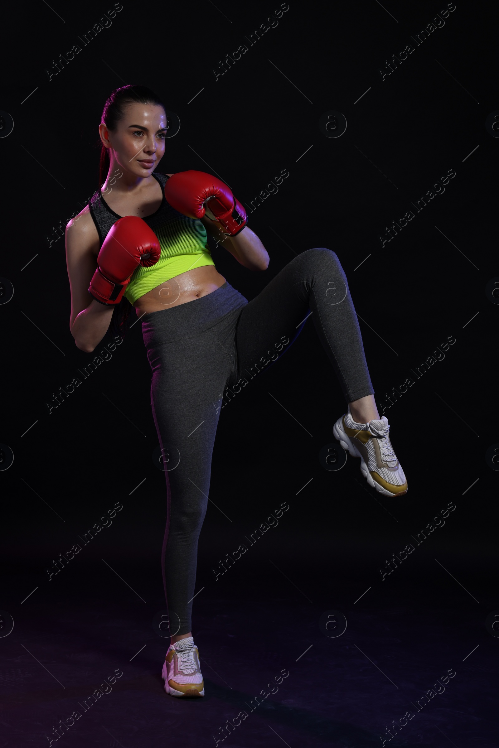 Photo of Beautiful woman in boxing gloves training on black background