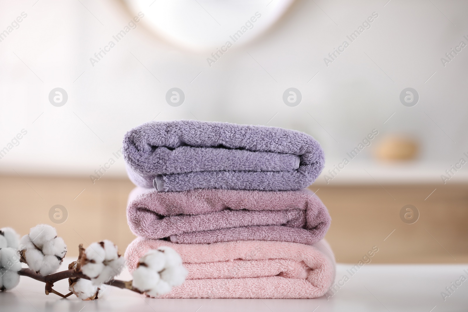 Photo of Stack of fresh towels and cotton flowers on table in bathroom