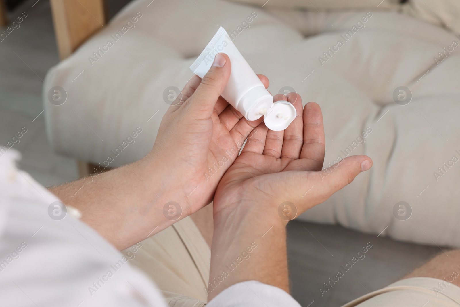 Photo of Man applying hand cream from tube at home, closeup