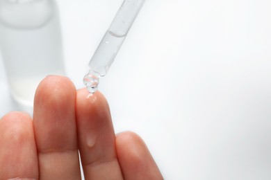 Woman dripping serum from pipette on her hand at white table, closeup. Space for text