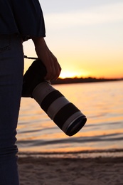 Photo of Female photographer with professional camera on riverside at sunset