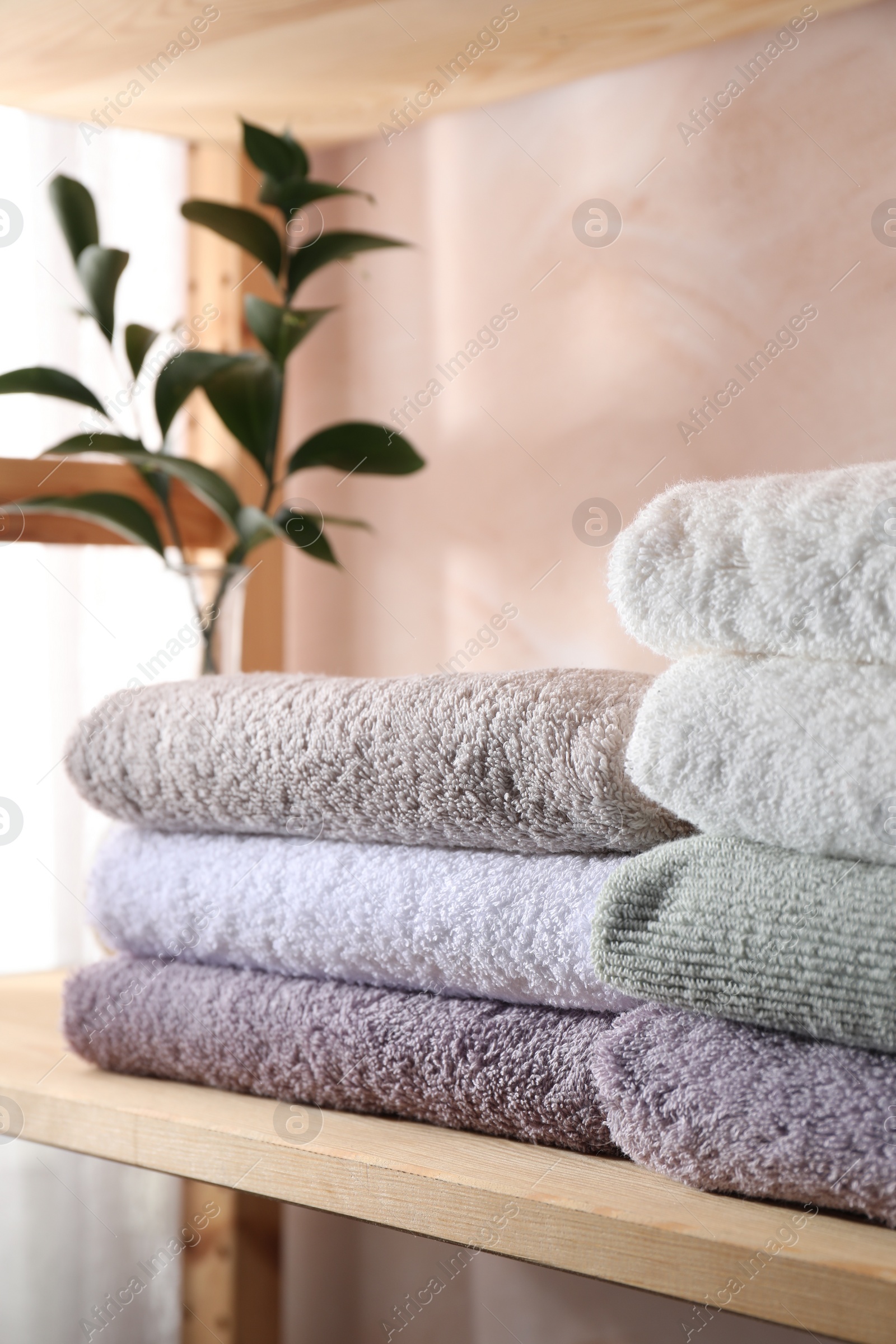 Photo of Stacked soft towels and green leaves on wooden shelf indoors