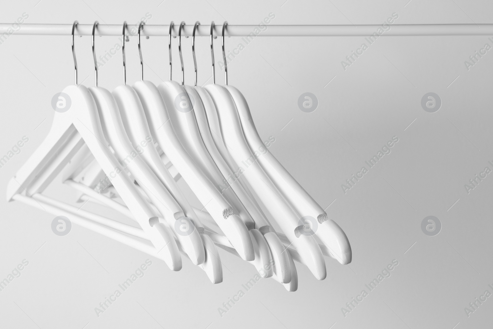 Photo of White clothes hangers on metal rail against light background