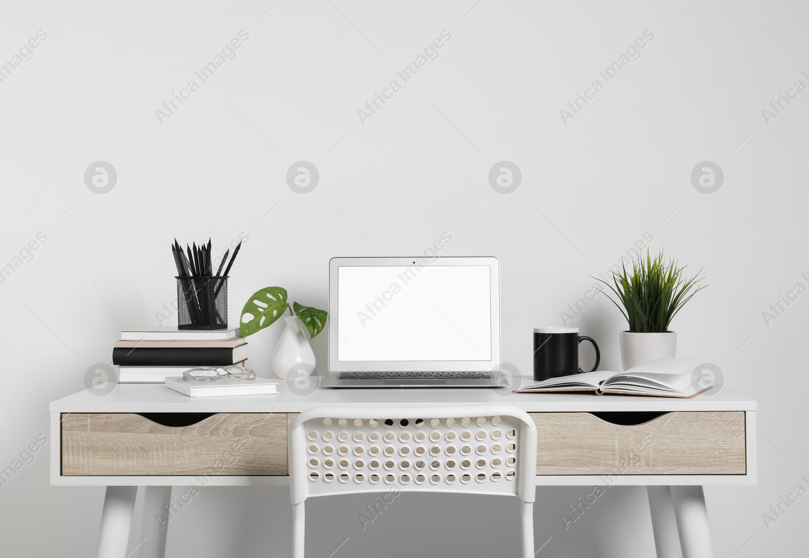 Photo of Cozy workspace with laptop, houseplants and stationery on wooden desk at home