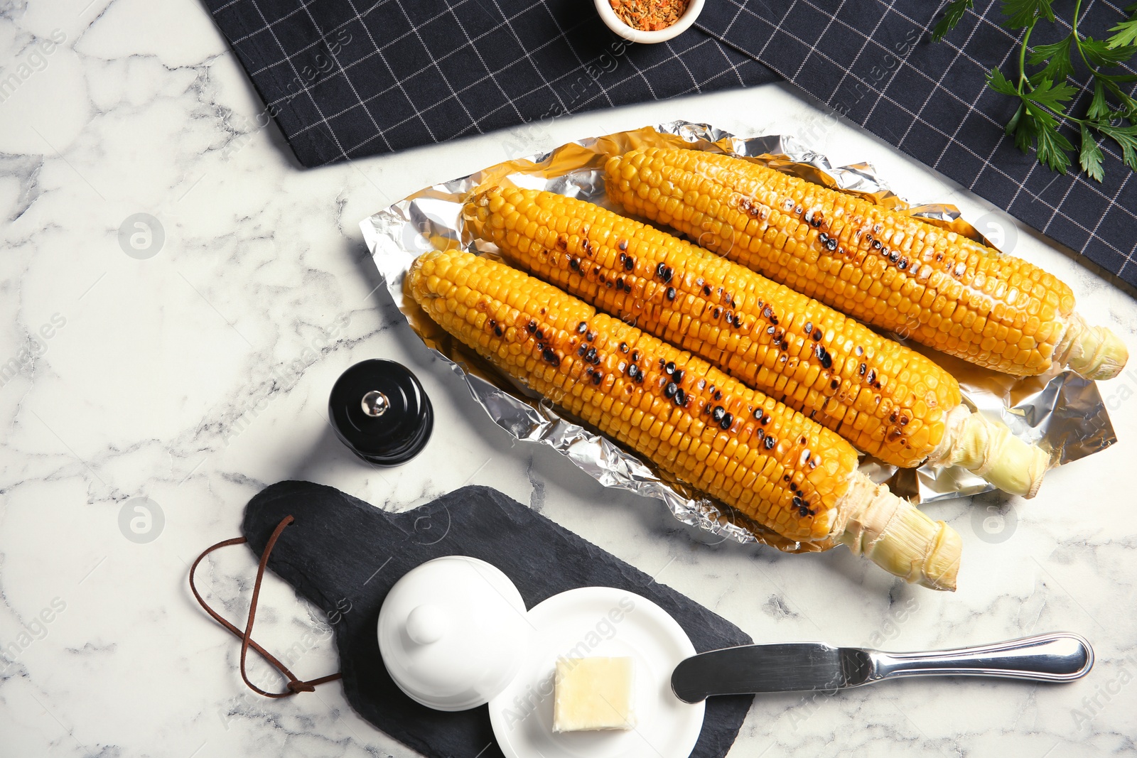 Photo of Fresh grilled tasty corn cobs served with butter on marble table, top view