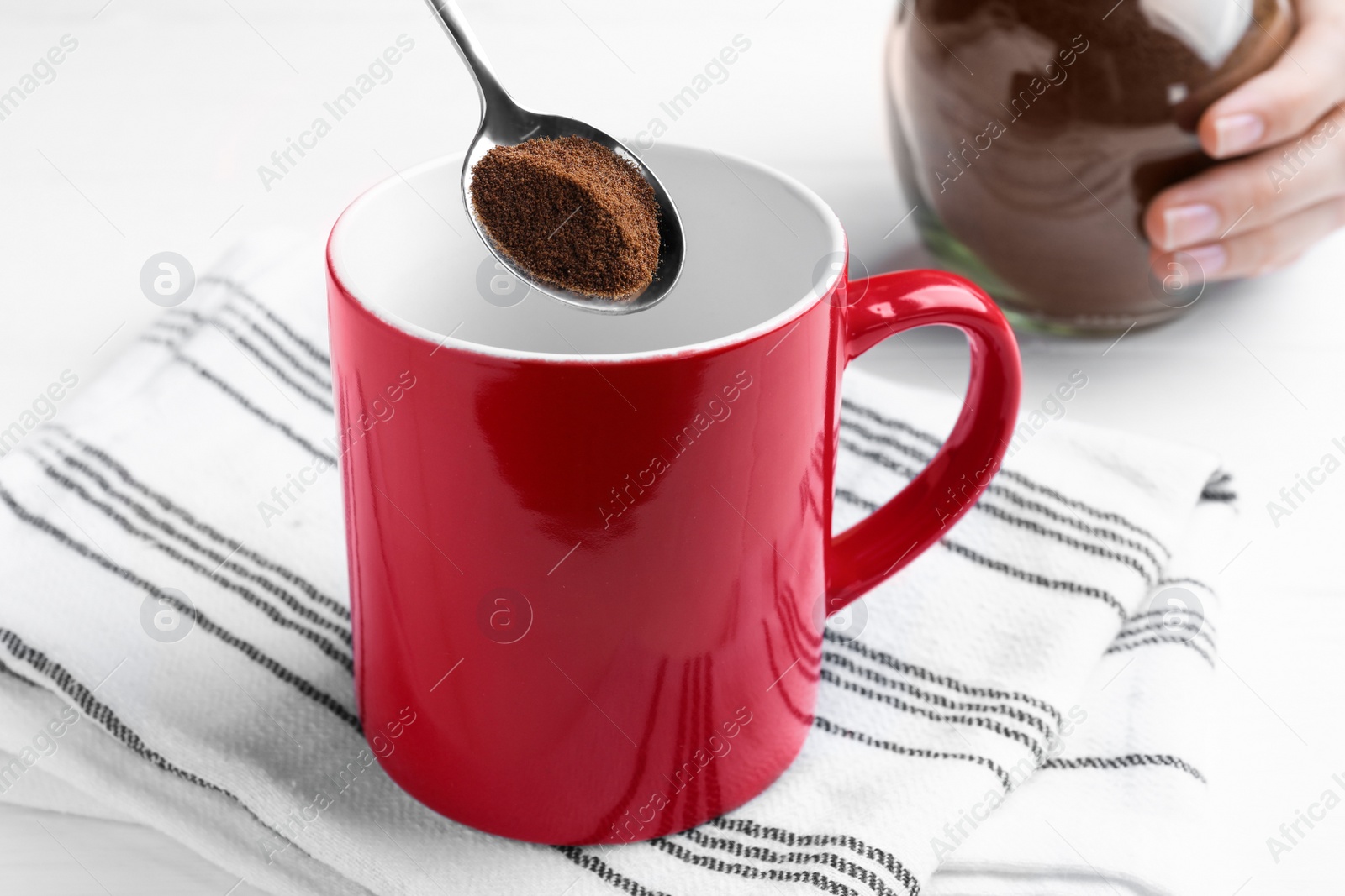 Photo of Woman pouring instant coffee into mug at white table, closeup