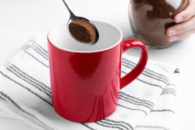 Photo of Woman pouring instant coffee into mug at white table, closeup