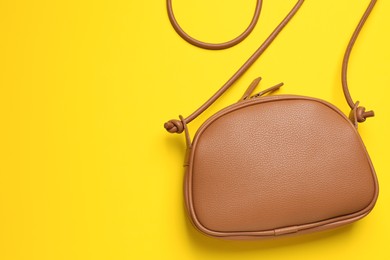 Photo of Stylish leather handbag on yellow background, top view. Space for text