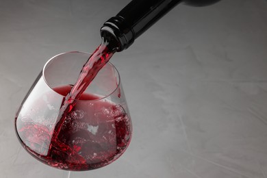 Pouring tasty red wine in glass at gray table, closeup. Space for text