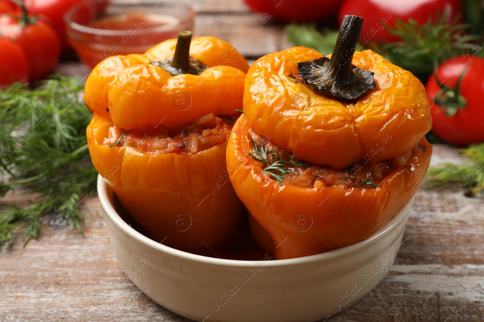 Photo of Tasty stuffed peppers in bowl on wooden table, closeup