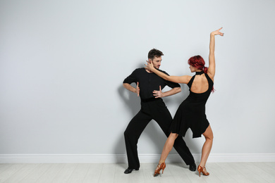 Photo of Beautiful young couple dancing near light wall. Space for text