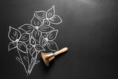 Photo of Golden bell and drawn flowers on black chalkboard, top view. School days