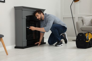 Photo of Man with screwdriver installing electric fireplace near wall in room