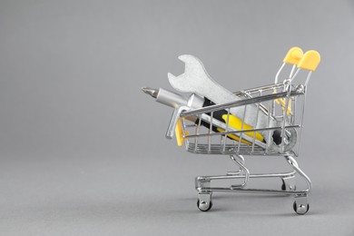 Photo of Small shopping cart with set of construction tools on grey background. Space for text