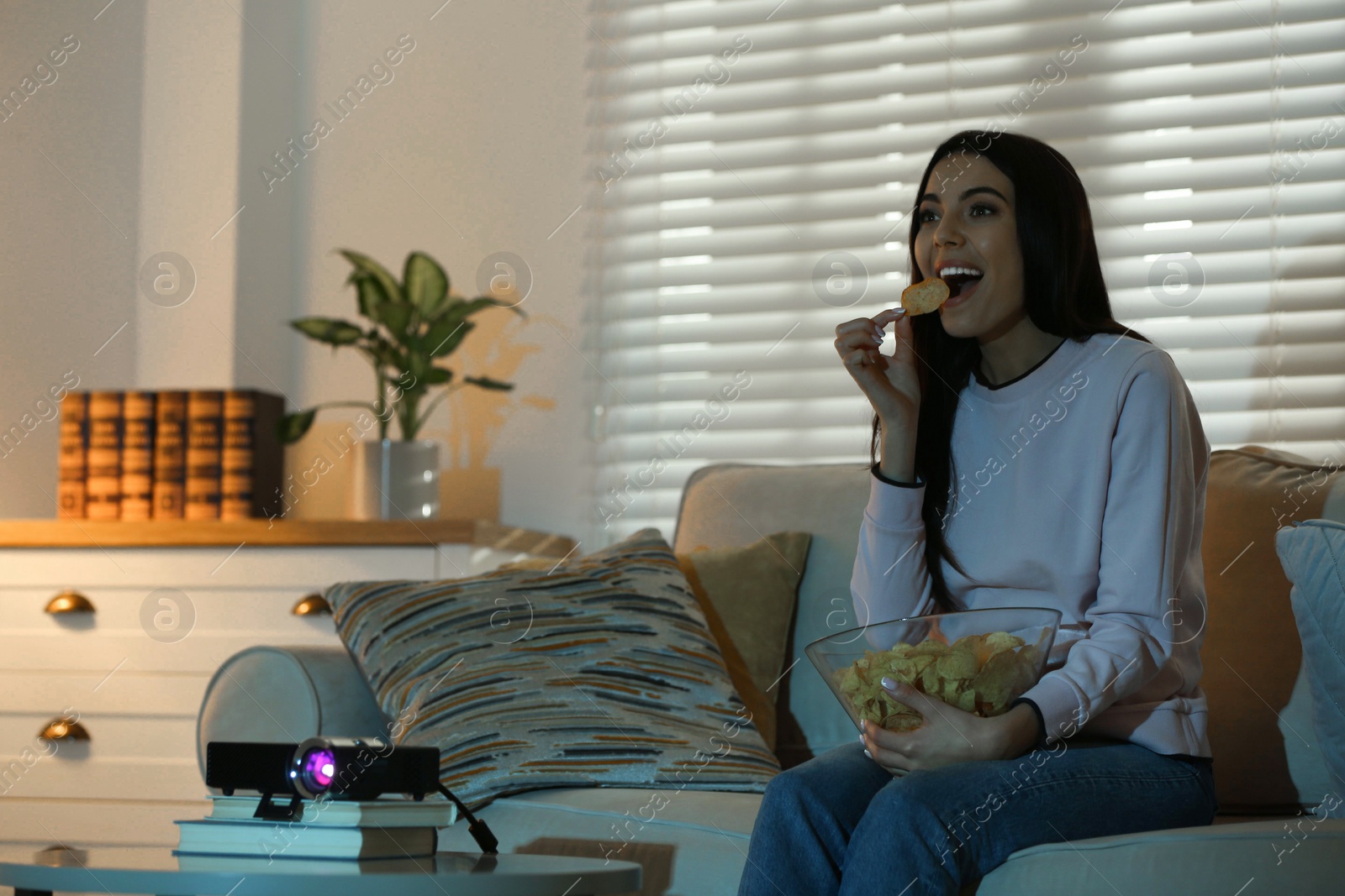 Photo of Young woman watching movie using video projector at home