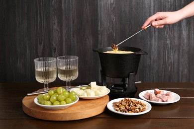 Photo of Woman dipping walnut into fondue pot with tasty melted cheese at white wooden table, closeup