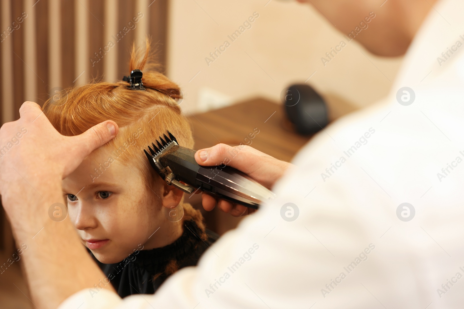 Photo of Professional hairdresser cutting boy's hair in beauty salon, closeup