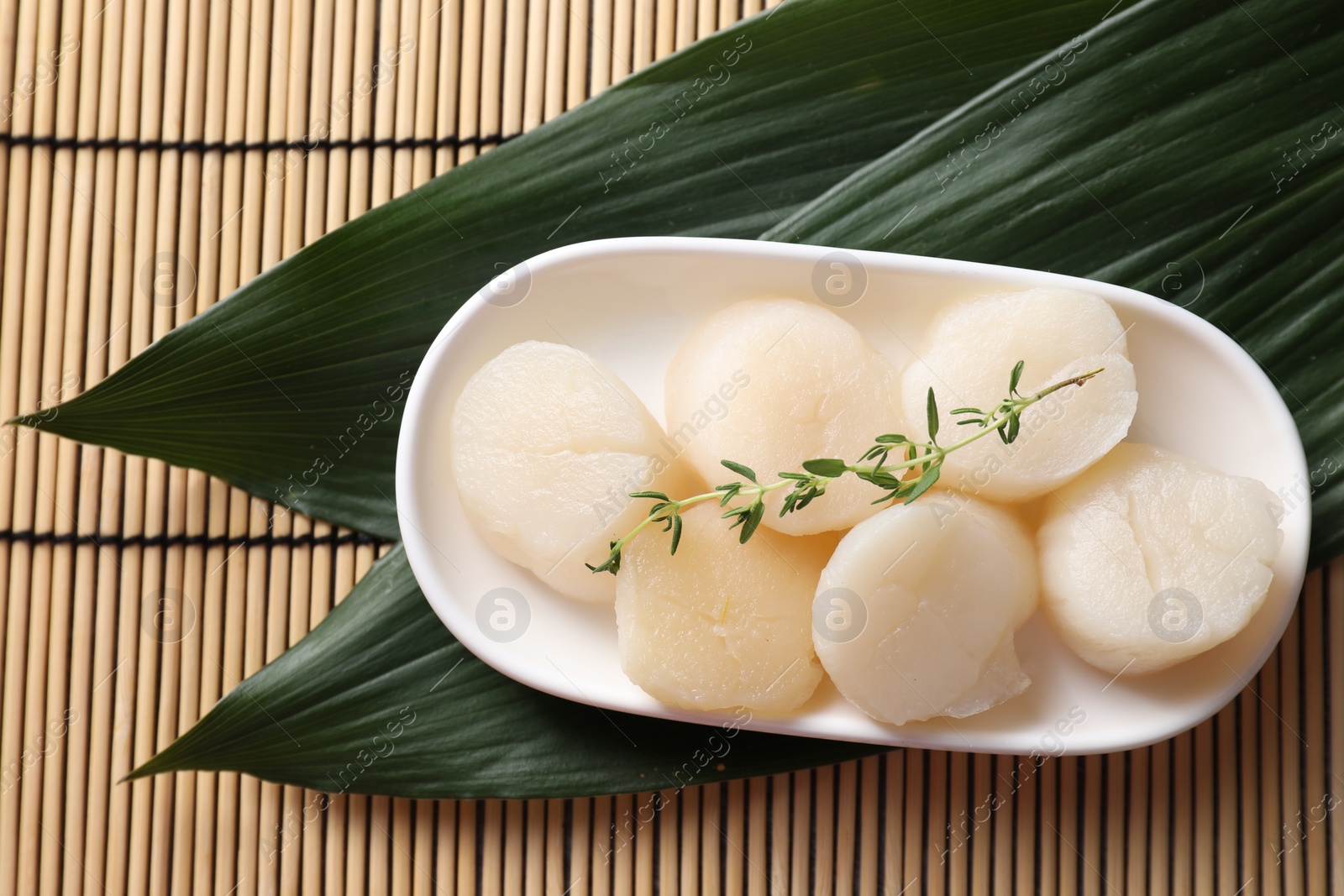 Photo of Fresh raw scallops, thyme and green leaves on bamboo mat, flat lay