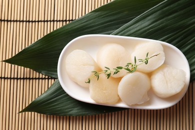 Photo of Fresh raw scallops, thyme and green leaves on bamboo mat, flat lay