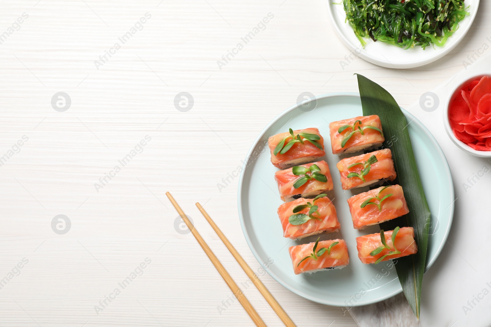 Photo of Tasty sushi rolls with salmon served on white wooden table, flat lay. Space for text