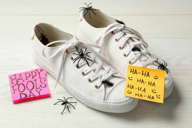 Photo of Shoes with fake spiders, bugs and Happy Fools' Day note on white wooden table
