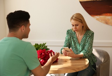 Photo of Young woman preferring smartphone over speaking with man during first date in cafe