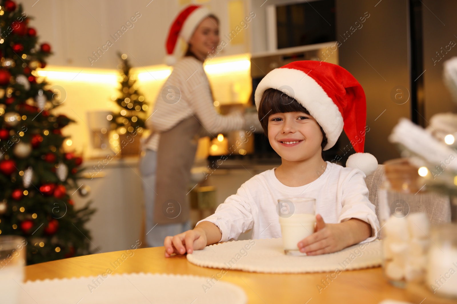 Photo of Cute little boy with glass of milk at table in kitchen. Christmas time