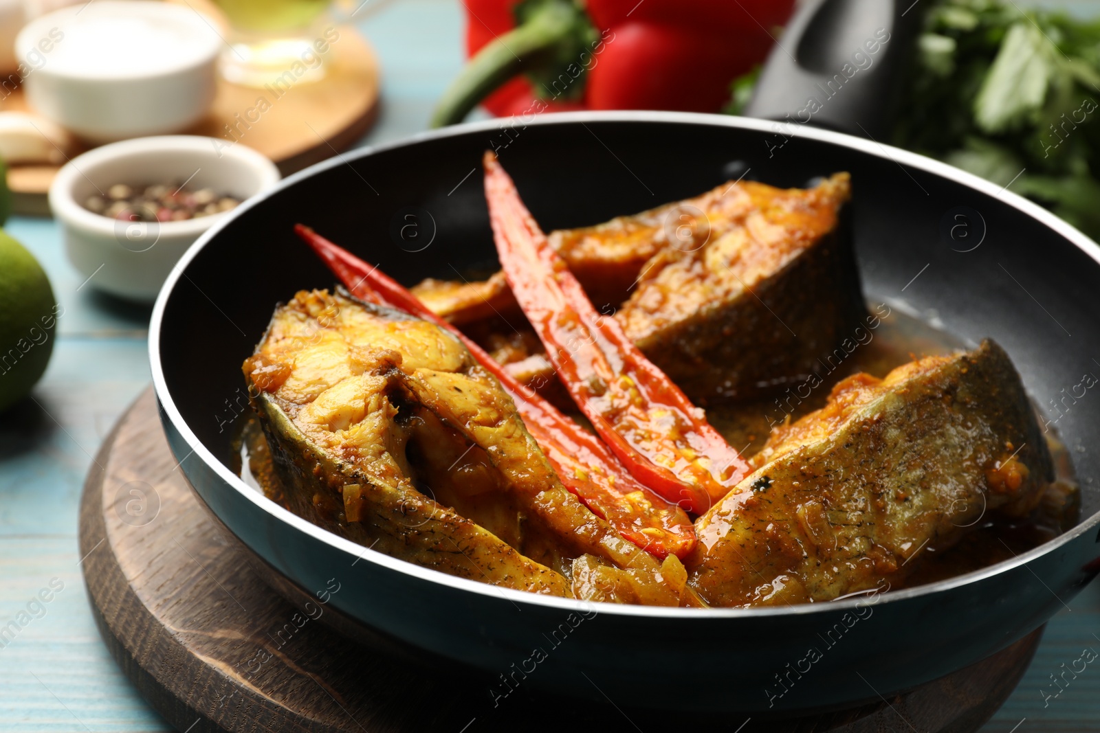 Photo of Tasty fish curry in frying pan and ingredients on light blue wooden table, closeup. Indian cuisine