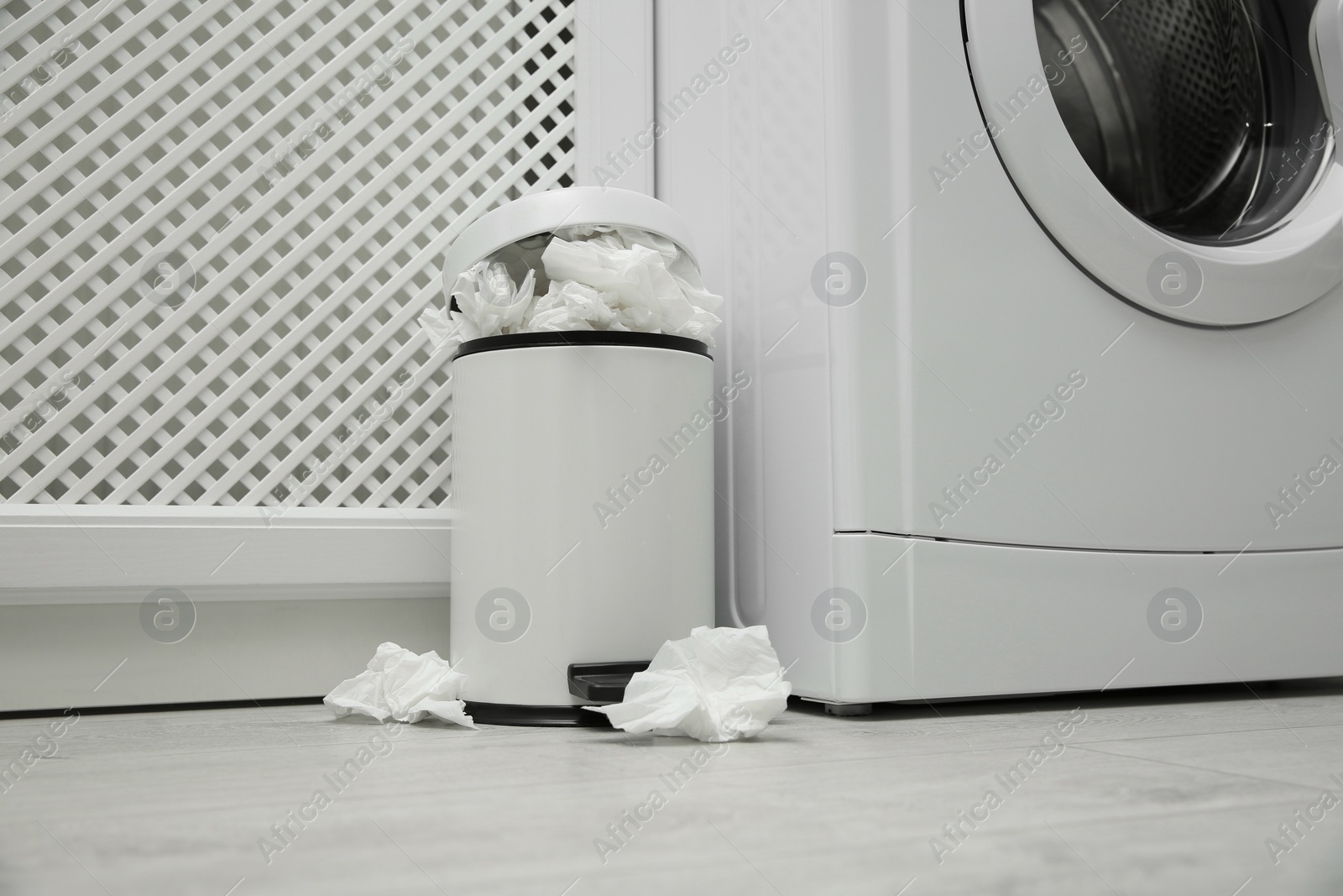 Photo of Used paper tissues in trash can near washing machine indoors