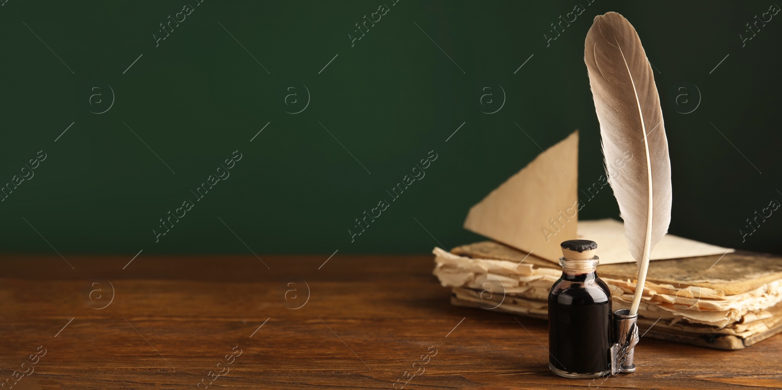 Image of Quill, bottle of ink and old book on wooden table, space for text. Banner design