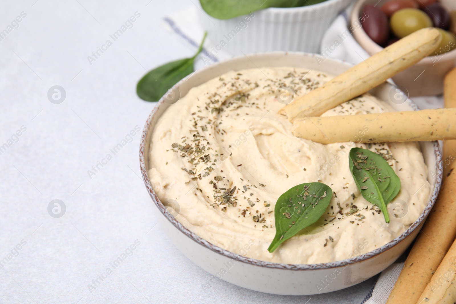 Photo of Delicious hummus with grissini sticks on light grey table, closeup. Space for text