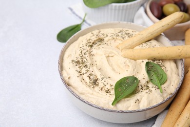 Delicious hummus with grissini sticks on light grey table, closeup. Space for text